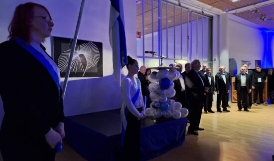 Suomenlippu ja kunniavartiasto. Taustalla näkyy sini-valkoisia ilmapalloja ja juhlapukuisia henkilöitä.